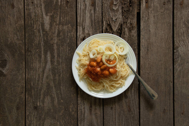 vařené vermicelli s fazolemi v rajčatech a cibulí v bílém talíři leží na dřevěné desce - Fotografie, Obrázek