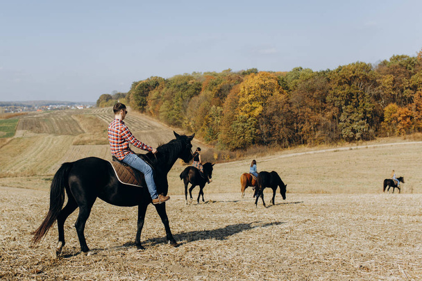 広いオープンフィールドと森を見下ろす後ろから乗馬。田舎の馬クラブで過ごすための無料の時間を楽しむ友人。趣味、スポーツ、リゾート、牧場のコンセプト. - 写真・画像