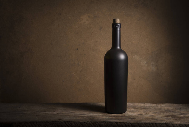 Cantinero o cavista masculino de pie cerca de los estantes de botellas de vino sostiene una copa de vino, mira el tinte y huele el sabor del vino en vidrio. - Foto, Imagen