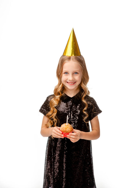 girl in a holiday cap in a black sequin dress holding a birthday cupcake - Photo, Image