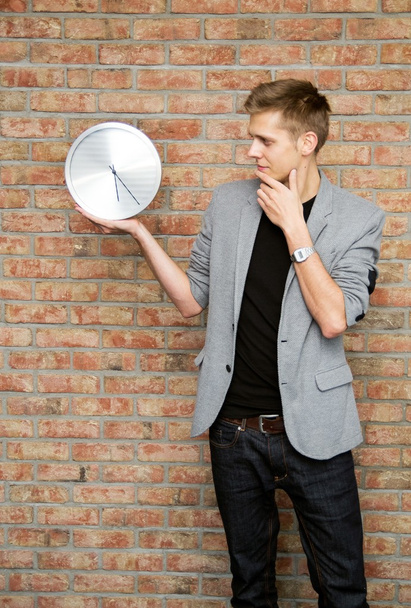 Young businessman holding a clock on brick wall background. - Фото, зображення
