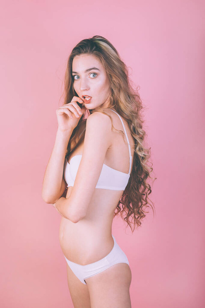young slim sexy girl in white sportswear posing on a pink background - Fotó, kép