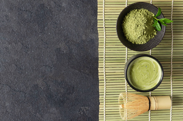 Green matcha tea drink and tea accessories on black background top view. Japanese tea ceremony concept. Chashaku spoon and chasen bamboo whisk for brewing matcha tea. - 写真・画像
