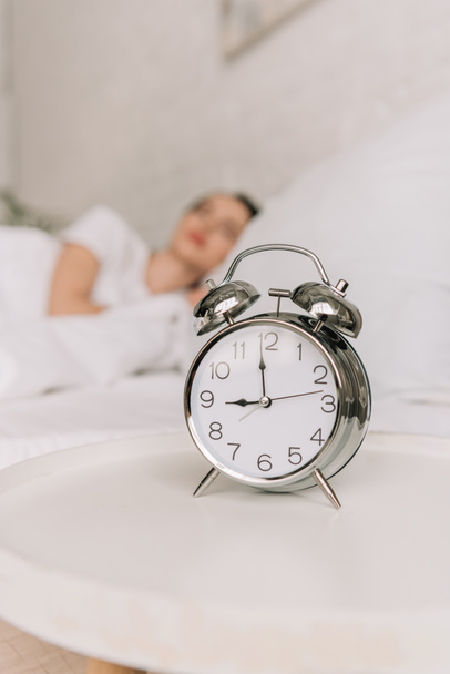 enfoque selectivo de reloj despertador vintage en la mesita de noche blanca y chica dormida en el fondo
 - Foto, imagen