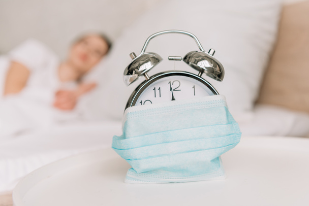 вибірковий фокус старовинного будильника, загорнутого в медичну маску і сплячу жінку на фоні
 - Фото, зображення