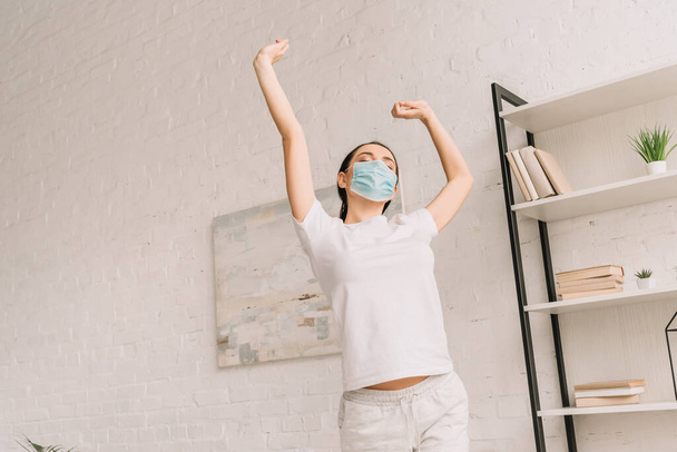 fiatal nő pizsamában és orvosi maszk nyújtja kezét a hálószobában - Fotó, kép