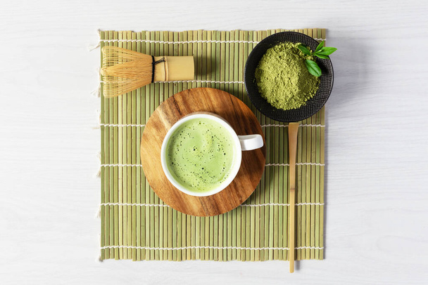 Organic green matcha tea and tea accessories on japanese mat on white wooden background. Japanese tea ceremony concept. Chashaku spoon and chasen bamboo whisk for brewing matcha tea. - Foto, Imagem