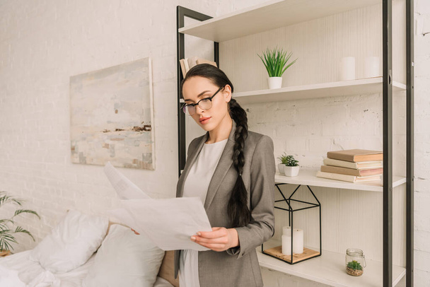 attentive businesswoman in blazer over pajamas looking at camera while standing in bedroom - Photo, image