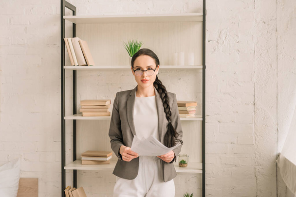 sebevědomá podnikatelka v blejzru přes pyžamo držící papíry při pohledu do kamery - Fotografie, Obrázek