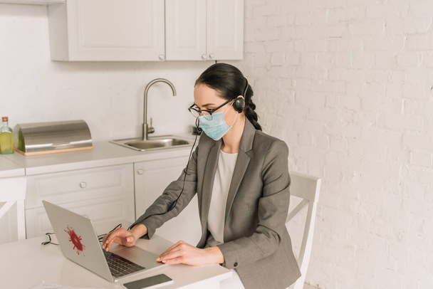 fiatal üzletasszony orvosi maszk gépelés laptop koronavírus matrica a konyhában - Fotó, kép