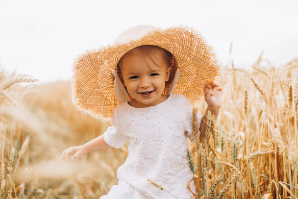 pretty cute baby girl with a beautiful smile wearing summer straw hat in a walk in the  wheat fields. selective focus. family, people concept - Valokuva, kuva
