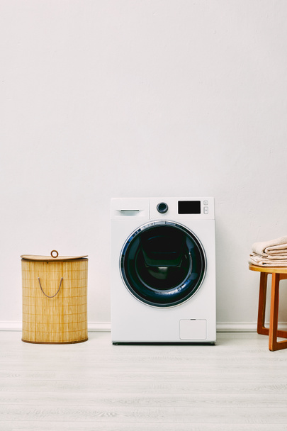 modern washing machine near laundry basket and coffee table with towels in bathroom  - Фото, зображення