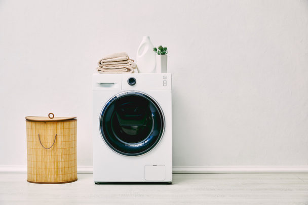 detergent bottle, towels and plant on washing machine near laundry basket in bathroom  - Fotó, kép