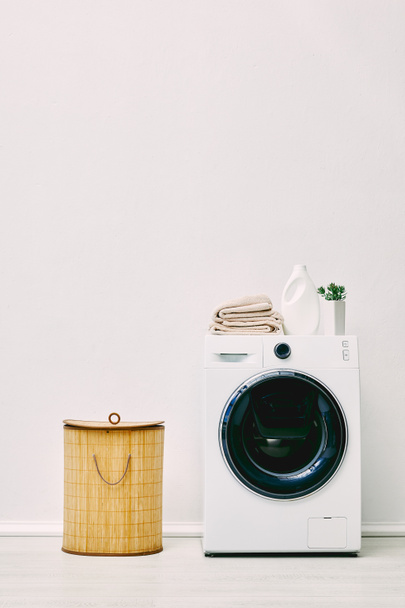 detergent bottle, towels and green plant on modern washing machine near laundry basket in bathroom  - 写真・画像