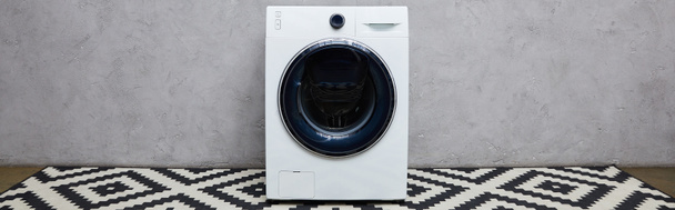 панорамний знімок сучасної пральної машини біля сірої стіни та декоративного килима у ванній
  - Фото, зображення