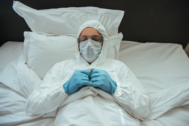 hombre en traje de hazmat, máscara médica y gafas de dormir en el dormitorio
  - Foto, Imagen