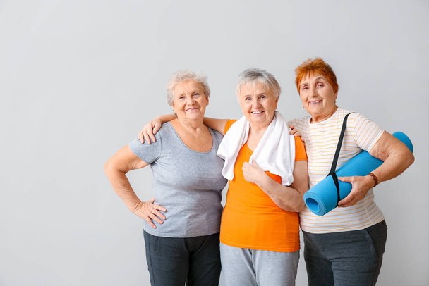 Glückliche ältere Frauen mit Yogamatte auf hellem Hintergrund - Foto, Bild