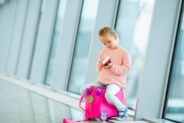 Urocza dziewczynka na lotnisku z bagażem czeka na wejście na pokład. - Zdjęcie, obraz