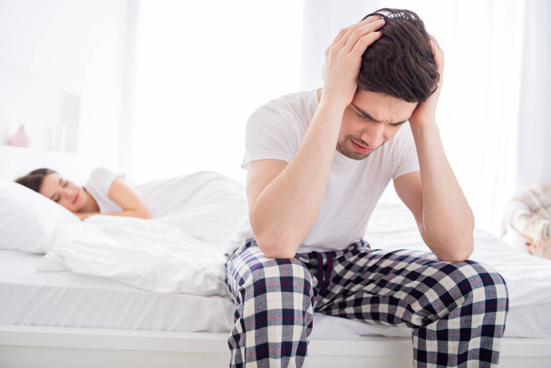 Фото розчарованого чоловіка сидить ліжко страждає мігрень голова біль не може спати його дружина хропіти апное в гучному одязі біла футболка піжами в будинку в приміщенні
 - Фото, зображення