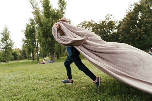 Веселый мальчик, бегающий в парке под одеялом. - Фото, изображение