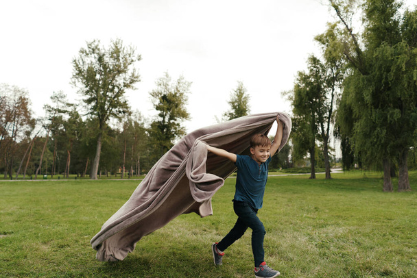 Garçon joyeux courant avec une couverture volante dans le parc - Photo, image