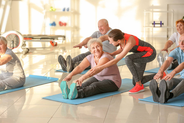 Young trainer helping elderly people during training in gym - Foto, immagini