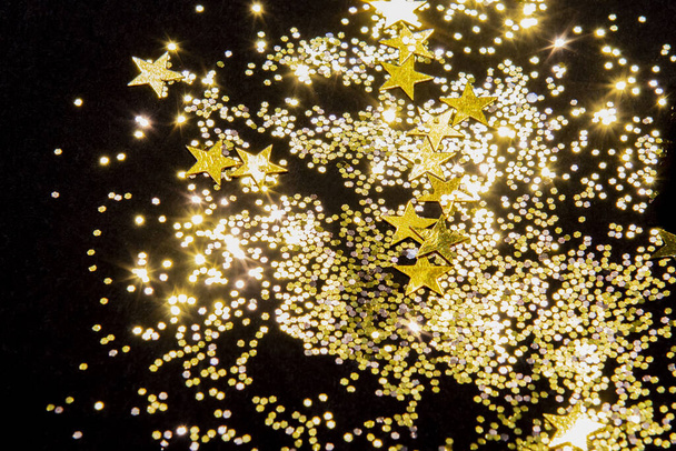 Gold glänzendes Glitzern und Sternkonfetti auf schwarzem Hintergrund - Foto, Bild