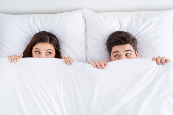 High angle above view photo of pretty lady husband guy couple lying sheets bed covering blanket faces morning romantic playful look eyes honeymoon wear pajama room indoors - Foto, imagen