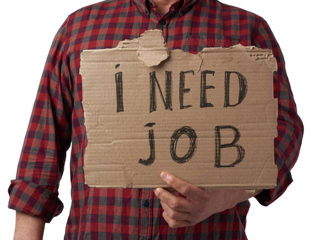 hombre en una camisa a cuadros y jeans sostiene un pedazo de papel con la inscripción que necesito trabajo, concepto de desempleo en el contexto de la crisis global, empleado despedido, hombre está aislado en un blanco
 - Foto, Imagen