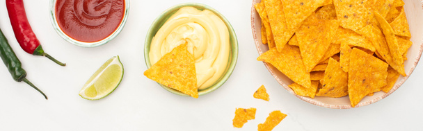 vrchní pohled na kukuřičné nachos s limetkou, chilli papričkami, kečupem a sýrovou omáčkou na bílém pozadí, panoramatický výstřel - Fotografie, Obrázek