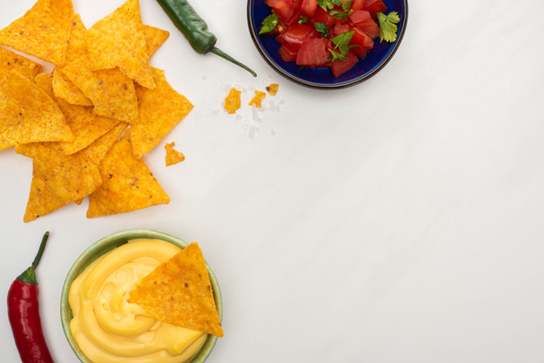 top view of corn nachos with chili and cheese sauce on wooden cutting board on white background - Foto, Imagem