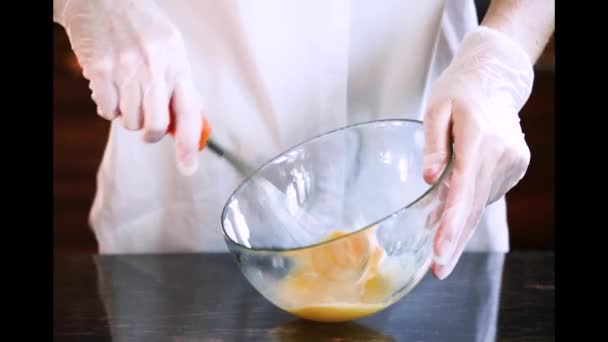 Las manos de las mujeres con guantes batiendo huevos en un tazón transparente
 - Metraje, vídeo