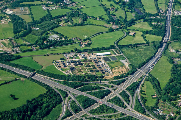 Uitzicht vanaf een vliegtuig van de Thorpe Interchange kruising tussen de M25 en M3 snelwegen in Zuidwest Londen. A Thames Water rioolwaterzuiveringsinstallatie ligt direct naast de drukke wegen in Virginia Water, Surrey. - Foto, afbeelding