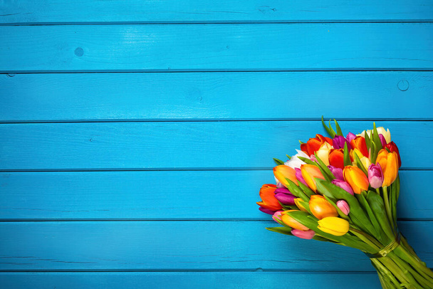 Colorful bouquet of tulips on blue wooden background. Spring flowers. Greeting card with copy space for Valentine's Day, Woman's Day and Mother's Day. Top view. - Photo, image