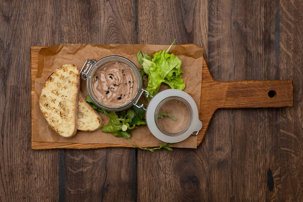 Chicken liver pate in the jar, ciabatta bread and salad mix on a rustic wooden board. - Fotografie, Obrázek