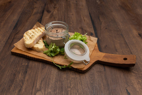 Chicken liver pate in the jar, ciabatta bread and salad mix on a rustic wooden board. - Fotografie, Obrázek
