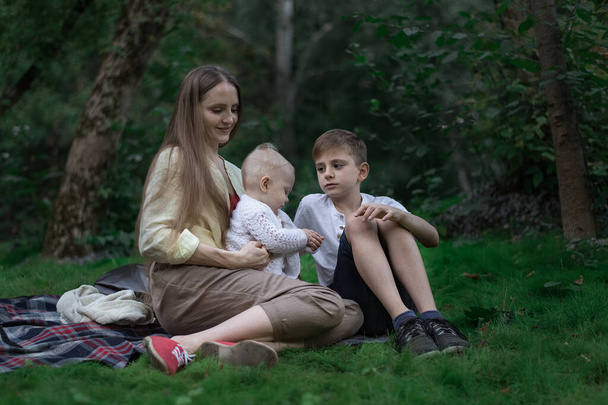 Picnic familiar en el jardín del parque al aire libre. Madre, hijo mayor y niño menor sentado en una manta de picnic
. - Foto, Imagen