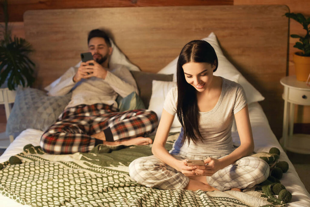 Jeune couple avec téléphones mobiles sur le lit à la maison
 - Photo, image