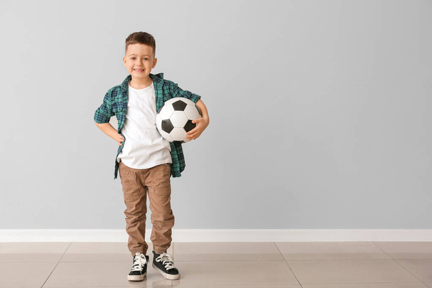 Happy little boy with soccer ball near grey wall - Фото, изображение