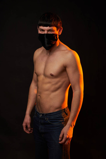 jovem muscular em máscara médica preta no fundo preto
 - Foto, Imagem
