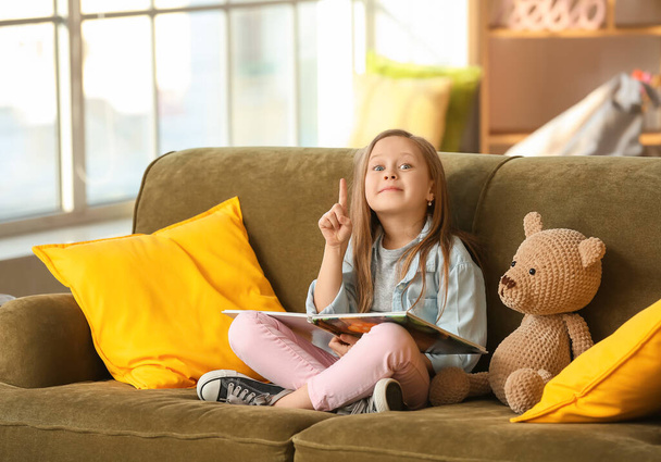 Cute little girl czytania książki na kanapie w domu - Zdjęcie, obraz