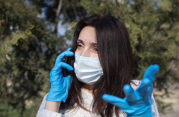 Νεαρή γυναίκα με ιατρική μάσκα με κινητό τηλέφωνο επικοινωνεί συναισθηματικά και χειρονομίες - Φωτογραφία, εικόνα