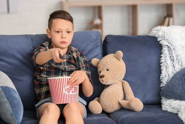 Söpö pikkupoika syö popcornia ja katsoo televisiota kotona.
 - Valokuva, kuva
