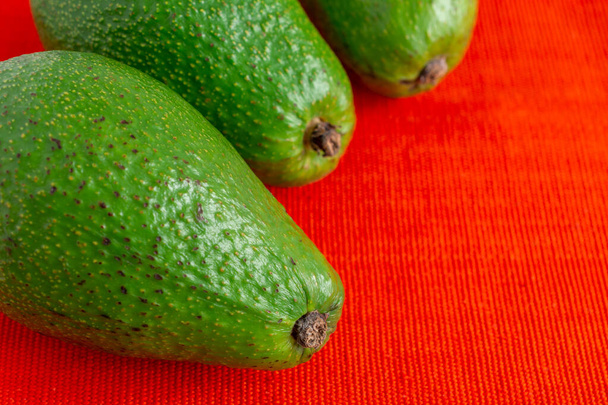 Aerial view of green avocados, with selective focus, on red tablecloth horizontally, with copy space - Photo, Image