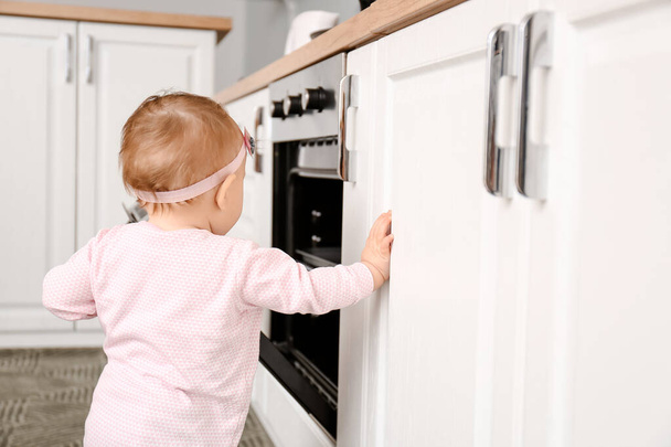 Μικρό μωρό κοντά στο φούρνο στην κουζίνα. Το παιδί κινδυνεύει. - Φωτογραφία, εικόνα