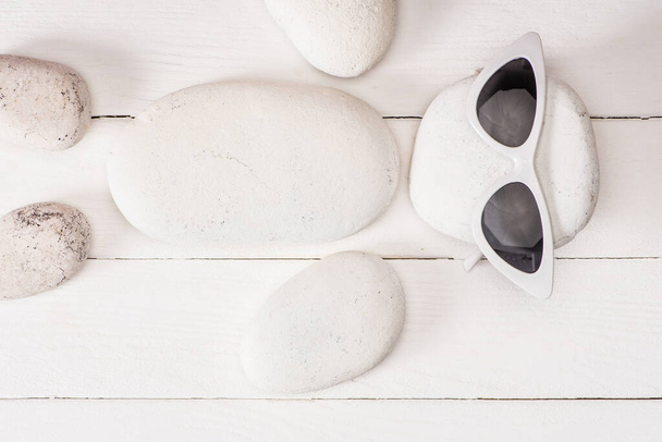 Κάτοψη από πέτρες στη θάλασσα με γυαλιά ηλίου σε λευκή ξύλινη επιφάνεια - Φωτογραφία, εικόνα