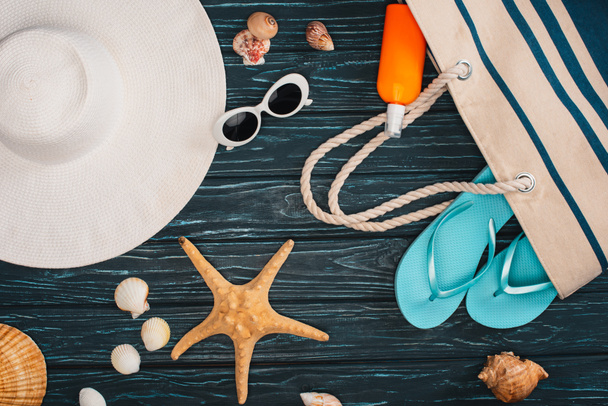Top view of sun hat near bag, flip flops and seashells on dark wooden surface - Foto, Imagem
