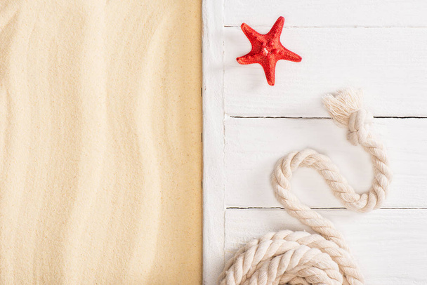 Top view of red starfish near rope on white wooden planks near sand - Foto, Bild