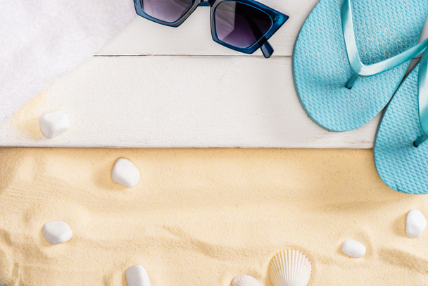 Top näkymä sininen varvassandaalit lähellä aurinkolasit ja pyyhe valkoinen puinen lankkuja lähellä kiviä hiekalla
 - Valokuva, kuva