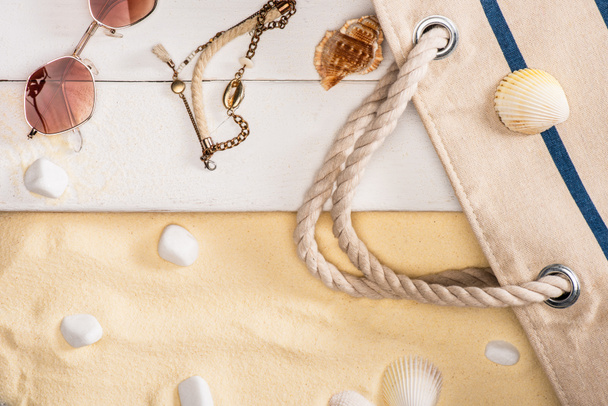 Top view of sunglasses, bracelet and bag on white wooden planks near pebbles on sand - Φωτογραφία, εικόνα
